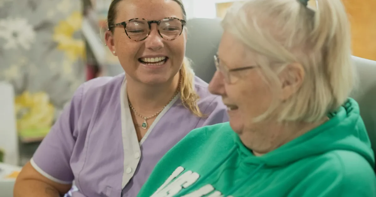 A care worker smiling beside an older woman.